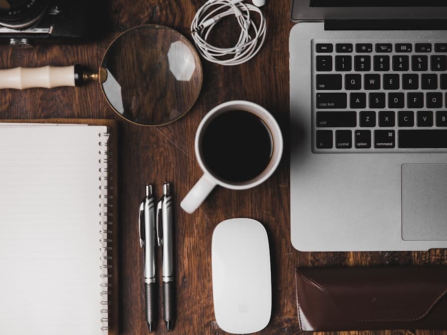 A magnifying glass, notebook and laptop laid out on a desk.